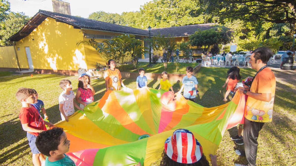 A joyful outdoor birthday party with children playing with a colorful parachute in a garden setting.